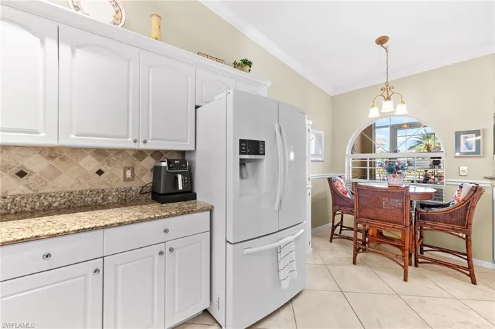 Kitchen with white cabinetry, white fridge with ice dispenser, ornamental molding, dark stone counters, and a chandelier