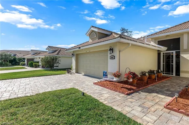 View of side of home featuring stucco siding, decorative driveway, an attached garage, and a yard