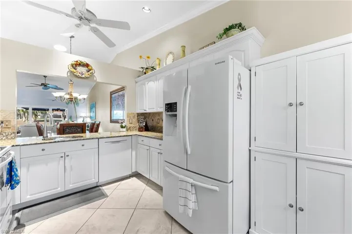 Kitchen featuring white appliances, white cabinetry, light stone countertops, a ceiling fan, and tasteful backsplash