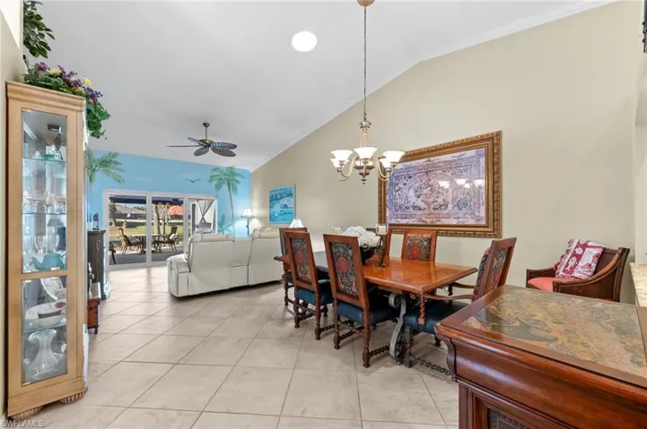 Dining space with crown molding, vaulted ceiling, ceiling fan, suspended lighting, and light tile patterned floors