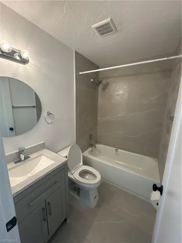 Bathroom featuring shower / bathtub combination, a textured wall, vanity, marble finish floors, and a textured ceiling