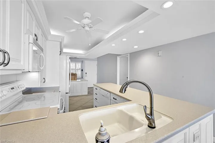 Kitchen with light countertops, white appliances, a raised ceiling, a sink, and ceiling fan
