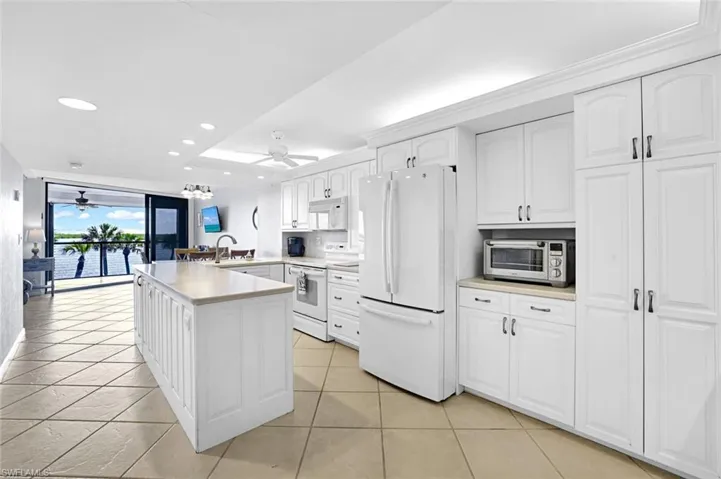 Kitchen with a sink, a ceiling fan, a peninsula, white appliances, and white cabinets