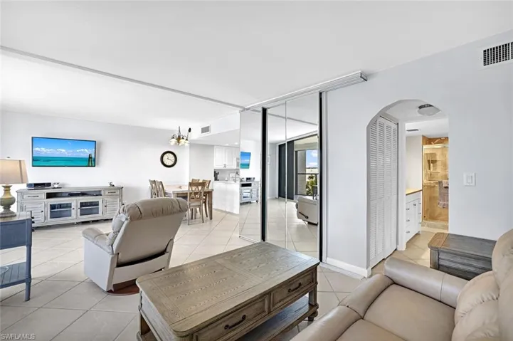 Living area featuring light tile patterned flooring, arched walkways, expansive windows, and visible vents