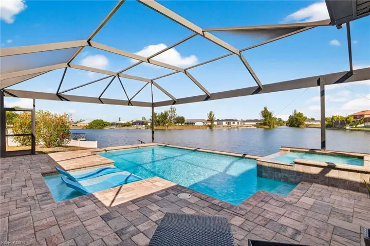 View of pool featuring a lanai, a water view, a sunroom, a pool with connected hot tub, and a patio area