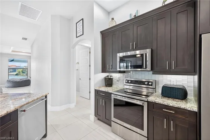 Kitchen with stainless steel appliances, dark brown cabinetry, arched walkways, light stone countertops, and decorative backsplash