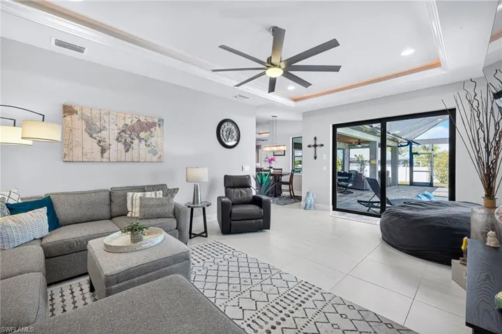 Living room featuring recessed lighting, tile patterned flooring, ceiling fan, ornamental molding, and a tray ceiling