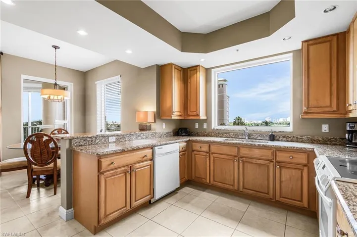 Kitchen with brown cabinets, white appliances, recessed lighting, light tile patterned flooring, and a peninsula