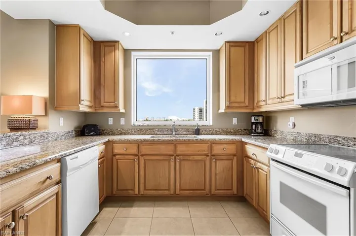 Kitchen featuring white appliances, light stone countertops, light tile patterned floors, brown cabinetry, and recessed lighting