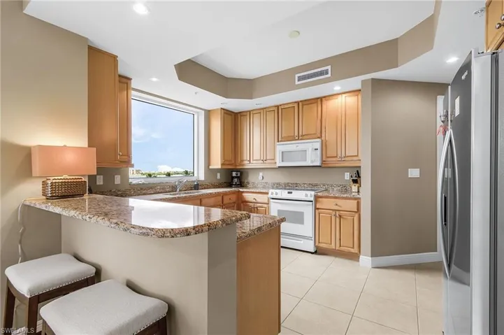 Kitchen featuring a peninsula, white appliances, light stone countertops, a breakfast bar, and light tile patterned floors
