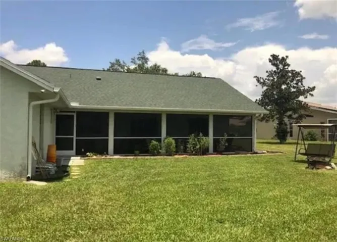 Back of house featuring a yard, a sunroom, stucco siding, and a shingled roof