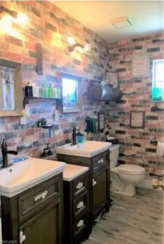 Bathroom featuring light wood-style flooring, brick wall, and two vanities