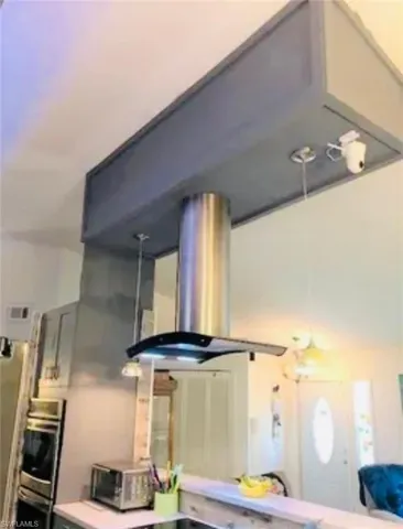 Kitchen view of island exhaust hood, double oven, and light countertops