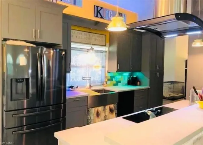 Kitchen with stainless steel fridge, exhaust hood, decorative light fixtures, black electric stovetop, and backsplash