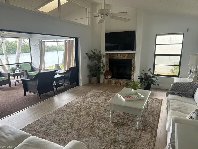 Living room featuring ceiling fan, a stone fireplace, lofted ceiling with skylight, wood ceiling, and hardwood / wood-style flooring