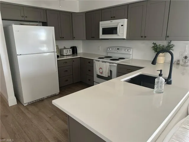 Kitchen with gray cabinetry, white appliances, wood-type flooring, sink, and kitchen peninsula
