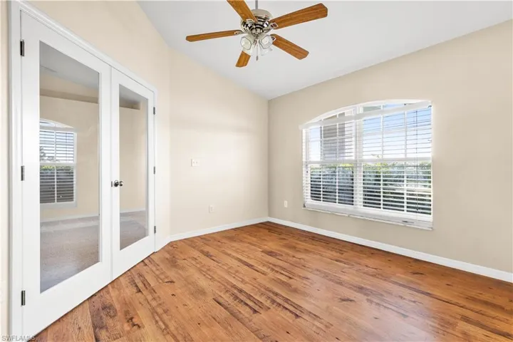 Empty room featuring hardwood / wood-style floors, ceiling fan, vaulted ceiling, and french doors