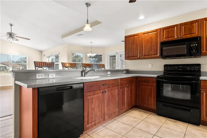 Kitchen featuring kitchen peninsula, a wealth of natural light, black appliances, and decorative light fixtures