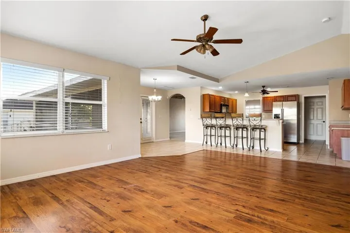 Unfurnished living room with ceiling fan with notable chandelier, light hardwood / wood-style flooring, and vaulted ceiling