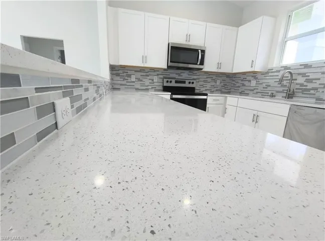 Kitchen with appliances with stainless steel finishes, white cabinetry, decorative backsplash, and light stone counters