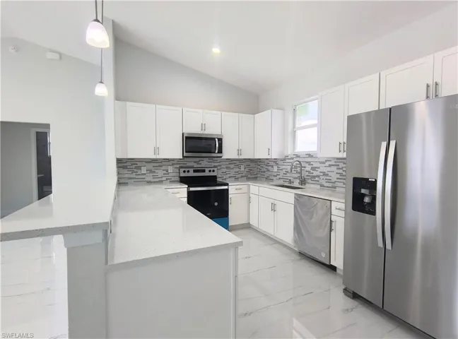 Kitchen with appliances with stainless steel finishes, hanging light fixtures, backsplash, light tile patterned floors, and lofted ceiling