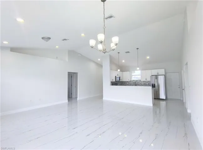 Unfurnished living room with high vaulted ceiling, a notable chandelier, and light tile patterned floors