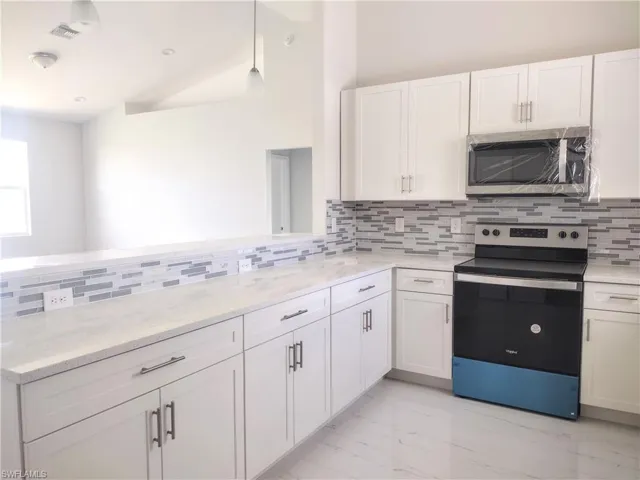 Kitchen with light stone counters, tasteful backsplash, white cabinetry, appliances with stainless steel finishes, and pendant lighting