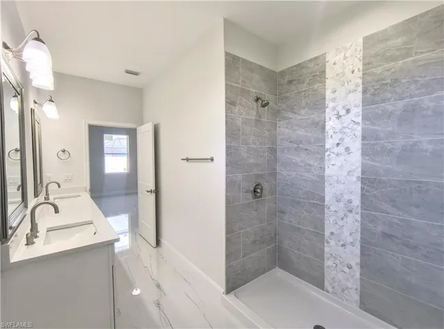Bathroom featuring tiled shower and dual bowl vanity