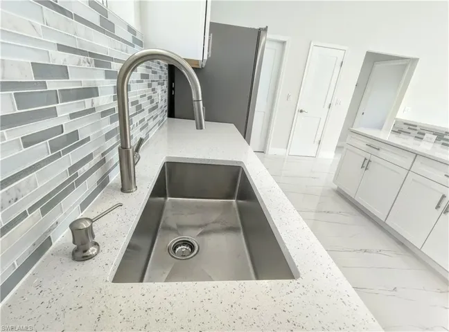 Details featuring white cabinets, decorative backsplash, sink, light stone counters, and light tile patterned floors