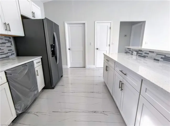 Kitchen featuring decorative backsplash, white cabinetry, light tile patterned flooring, and light stone countertops