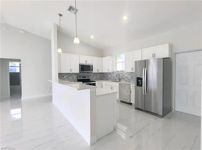 Kitchen with light tile patterned flooring, a wealth of natural light, white cabinets, appliances with stainless steel finishes, and pendant lighting