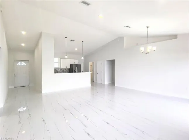 Unfurnished living room featuring high vaulted ceiling, a notable chandelier, and light tile patterned floors