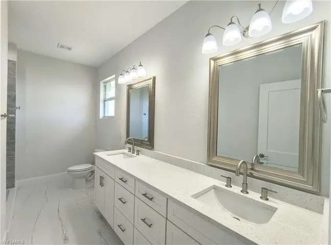 Bathroom with toilet, double sink vanity, and tile patterned flooring
