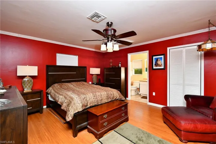 Bedroom featuring visible vents, baseboards, ornamental molding, light wood-style flooring, and a closet