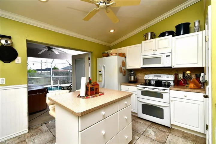 Kitchen featuring white appliances, white cabinetry, a ceiling fan, and ornamental molding