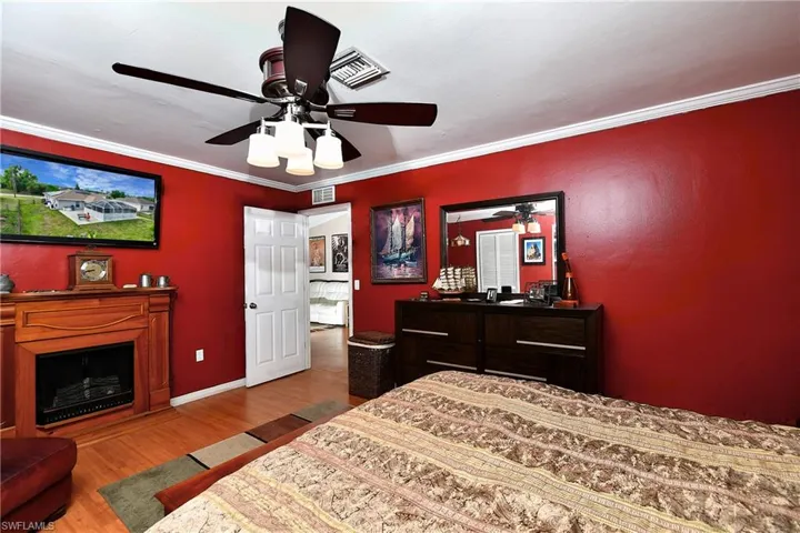 Bedroom with wood finished floors, baseboards, visible vents, ceiling fan, and crown molding