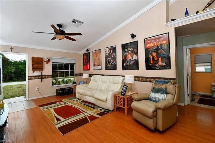 Living area featuring visible vents, wood finished floors, crown molding, lofted ceiling, and ceiling fan