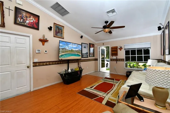 Living room with ceiling fan, wood finished floors, visible vents, and ornamental molding