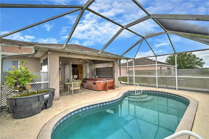 Outdoor pool featuring glass enclosure, a patio area, fence, and a hot tub