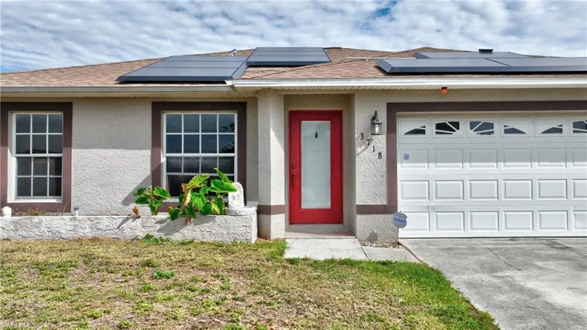 View of front of property featuring roof mounted solar panels, a garage, roof with shingles, and stucco siding