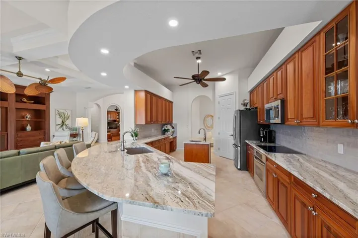 Expansive kitchen featuring a curved island with seating, natural stone countertops, warm wood cabinetry, and integrated stainless steel appliances