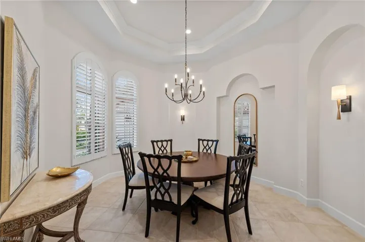 Formal dining space featuring a tray ceiling, arched window openings with plantation shutters, a chandelier, and sconce lighting