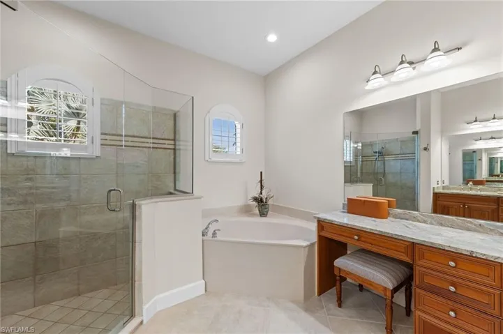 Spacious bathroom featuring a glass-enclosed shower, built-in soaking tub, and a vanity with a stone countertop and integrated makeup area