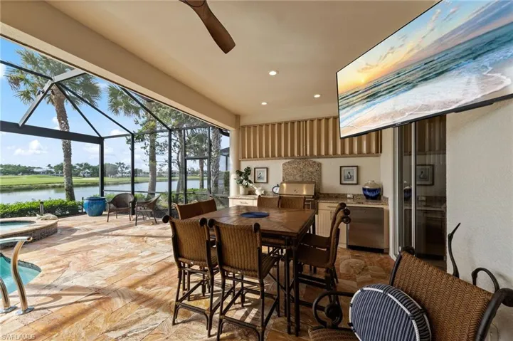 Screened lanai featuring a built-in outdoor kitchen with stainless steel appliances, a recessed ceiling fan, and stone tile flooring