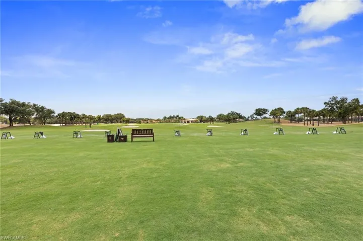 Expansive golf course with manicured green space, featuring multiple hitting bays, a wooden bench, and distant mature trees