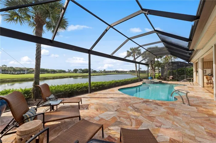 Screened lanai featuring a freeform swimming pool with integrated spa, expansive stone patio, and direct waterfront access