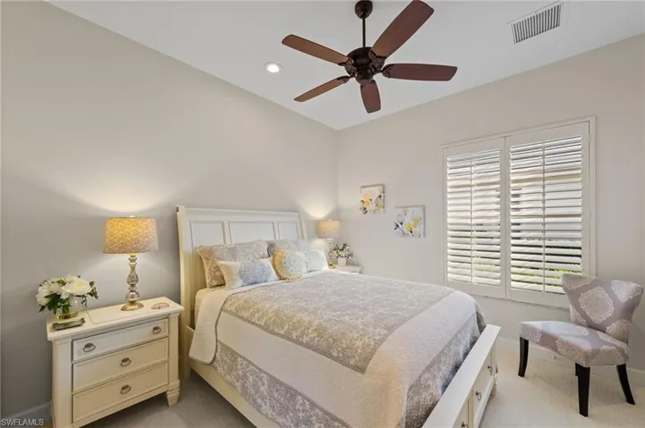 Interior room featuring a white paneled headboard, plantation shutters, recessed lighting, and a ceiling fan with dark wood-finish blades