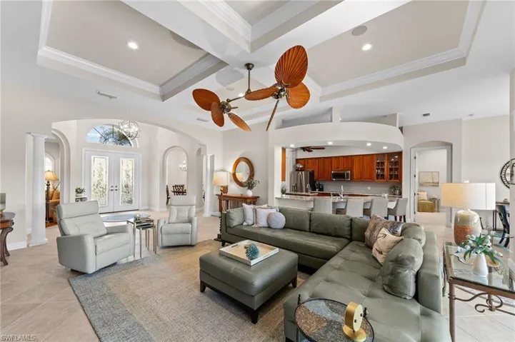 Spacious living area featuring coffered ceilings, tile flooring, and an open-concept design with arched entryways