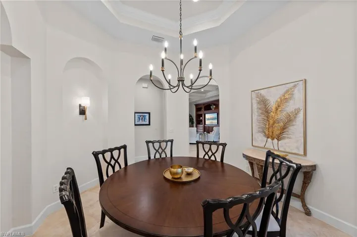 Tray ceiling with crown molding, chandelier lighting, arched wall niches, and sconce lighting