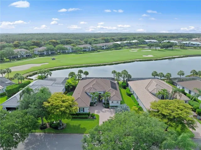 Mediterranean-style single-story residence featuring a tile roof, mature landscaping, an expansive driveway, and a private backyard bordering a water feature and golf course